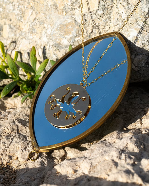 collier poulpe plaqué or présenté de près posé sur un miroir